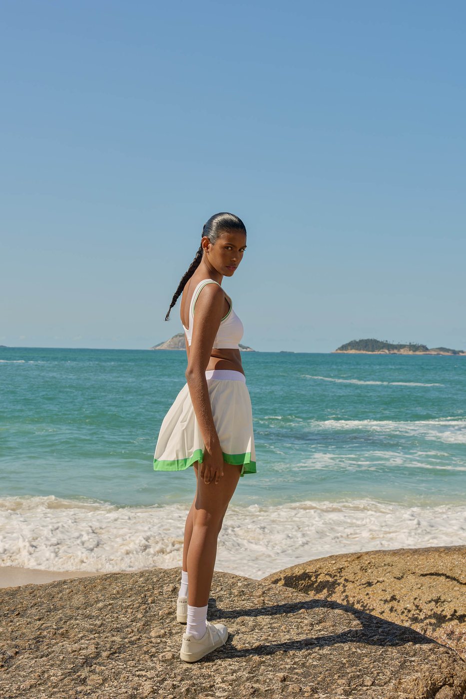 Mulher de saia esportiva branca com barra verde, de frente para o mar